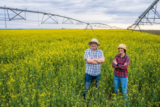 Proud two generations farmers are standing in their rapeseed field.