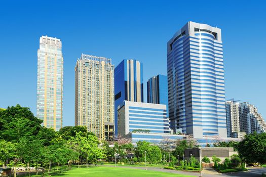 Skyscrapers and blue sky fill the background behind beautiful green grass and trees.