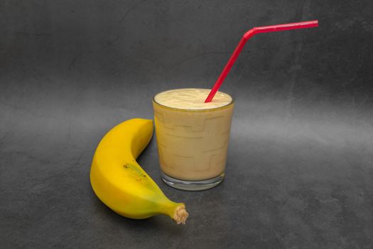 Milkshake with banana flavor and cocktail tube on dark background