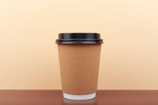 Disposable cardboard cup of coffee or tea on brown table against beige background with copy space. Concept of hot drinks for take away