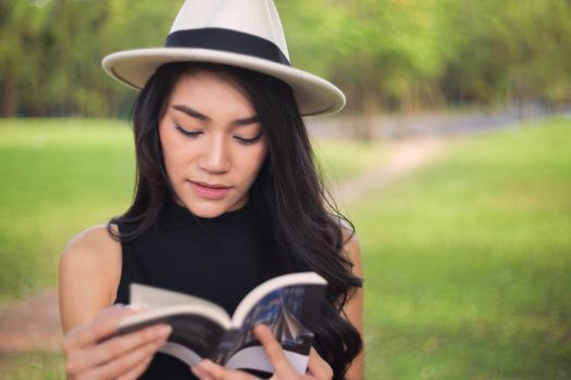 Attractive student teen girl reading book on green spring grass