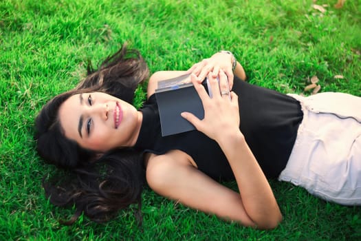 Attractive student teen girl reading book on green spring grass