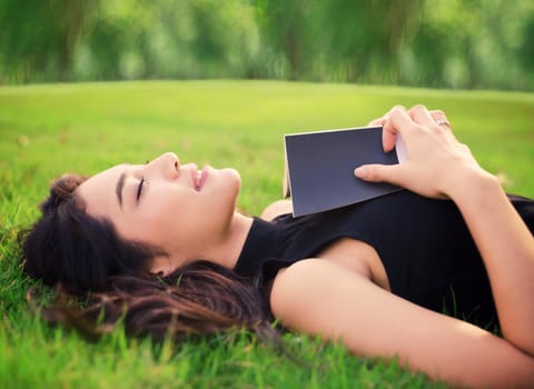 Attractive student teen girl reading book on green spring grass