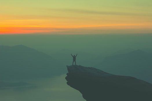 Young happy tourist on top of a mountain enjoying valley view before sunset.