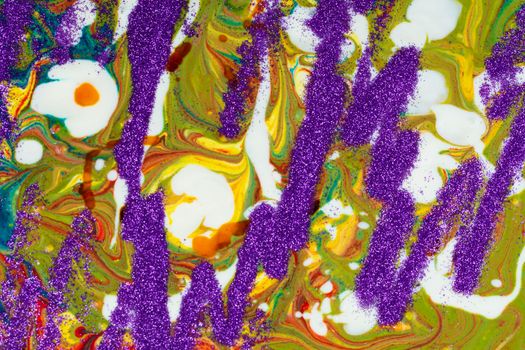 A background made up of many textures, shapes and materials. Purple sparkles are scattered on a multicolored acrylic background.