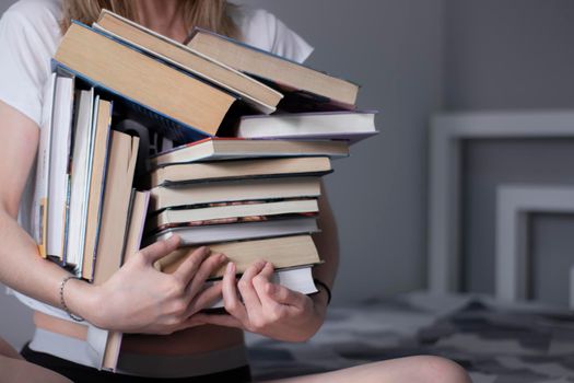 happy beautiful slim girl holds a lot of different books in her hands. Homeschooling. Studying in quarantine. Reading is helpful - horizontal photo