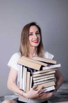 happy beautiful slim girl holds a lot of different books in her hands. Homeschooling. Studying in quarantine. Reading is helpful - vertical photo