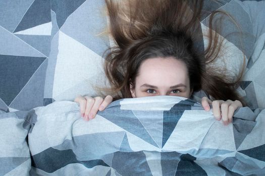 A slim girl in a bed is covering herself with a blanket - grey sheets and underwear