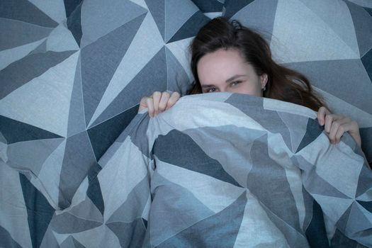 A slim girl in a bed is covering herself with a blanket - grey sheets and underwear