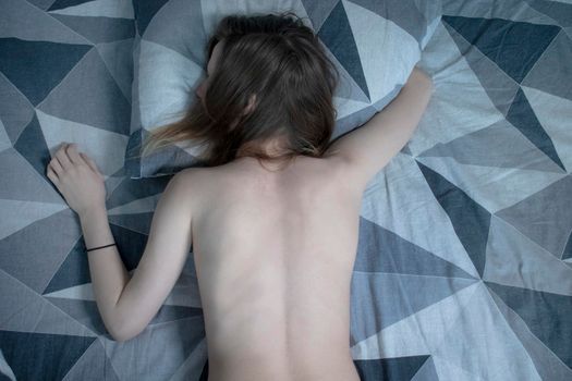 A slim girl in a bed sleeping, hugging a pillow - grey sheets and underwear