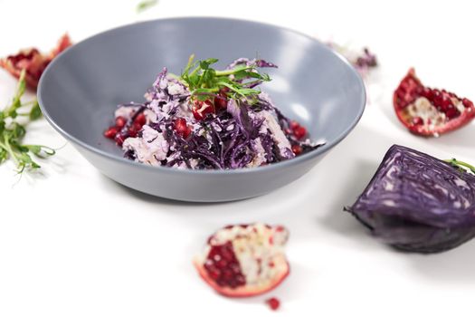 Close up of modern beautiful blue bowl with appetizing purple cabbage salad with juicy grenade on white background. Concept of process cooking with fresh vegetables at home.