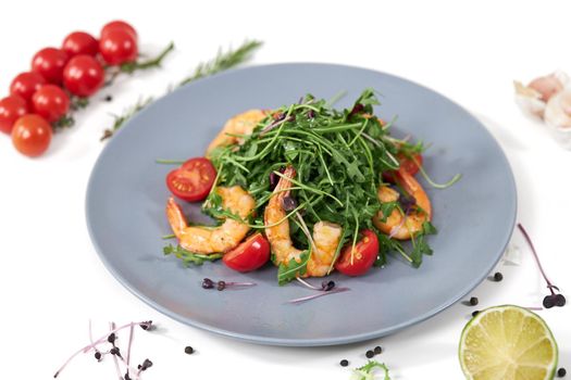 Close up of appetizing salad with fresh arugula,tomatoes cherry and juicy shrimps on white background. Concept of menu with the right products for weight loss.