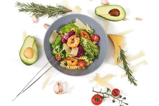 Top view of modern blue bowl with pasta,seafood,avocado,tomatoes and fresh leaf greens on white background. Concept of beautiful composition with vegetables and tasty cheese and herbs. 