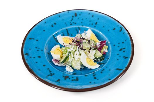 Close up of beautiful modern blue plate with delicious salad with vegetables and eggs on white background. Concept of appetizing salad with healthy vitamins for emaciation. 