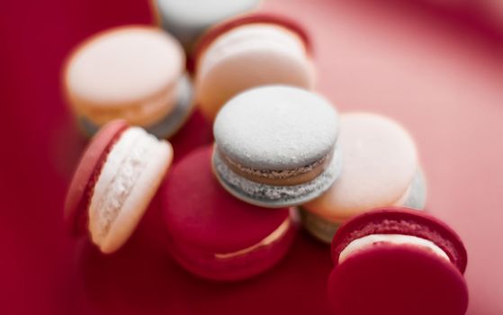 Pastry, bakery and branding concept - French macaroons on wine red background, parisian chic cafe dessert, sweet food and cake macaron for luxury confectionery brand, holiday backdrop design