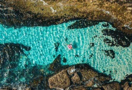 Female floating in a donut float ring toy in the ocean with idyllic crystal blue water