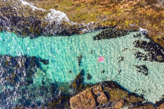 Woman laying relaxing in the sunshine  in a beautiful rock pool in a bright pink ring donut floaty