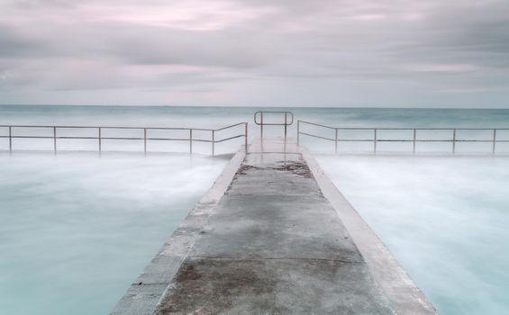 Twin cock pools with cement walkway between each.  Long exposure tidal overflows.  Austinmer beach Australia