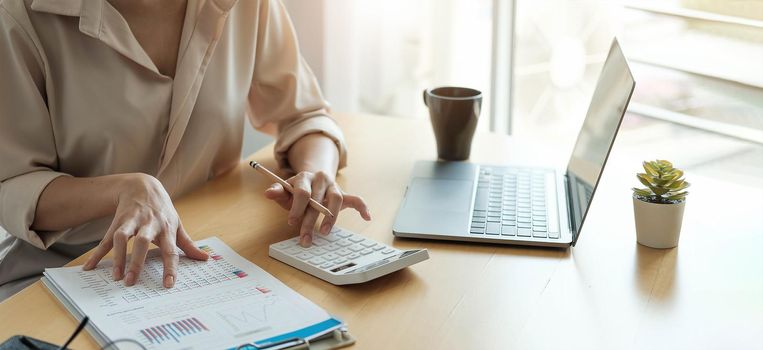 Business woman working in finance and accounting Analyze financial budget with calculator and laptop computer in the office.