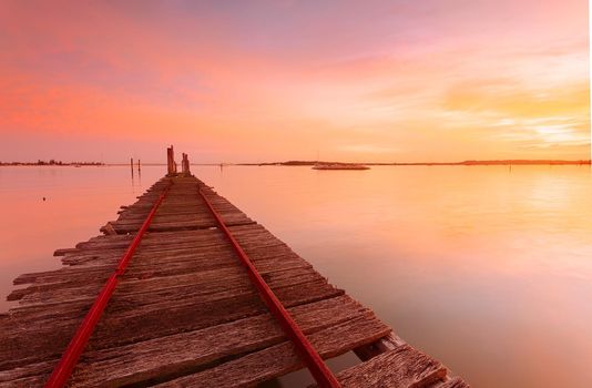 Sunrise sky and reflections at the old rustic timber  oyster jetty weathered timber planks with rusty nails protuding