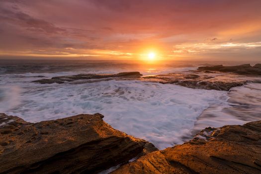 Beautiful morning with pretty sunrise sky with starburst from the risen sun as tidal flows create ocean  rock waterfalls