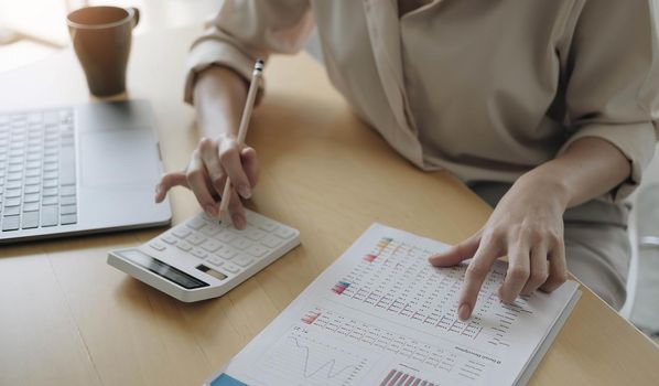 Business woman working in finance and accounting Analyze financial budget with calculator and laptop computer in the office.