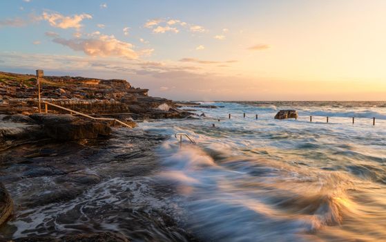 Early morning swimmers attempt to swim laps in turbulent ocean rock pool battered by waves in a high tide.
1/4 second expoosure, people and waves are in motion