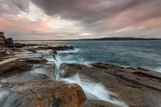 Waves surge up though a deep narrow chasm in  rocks near coast of Sydney