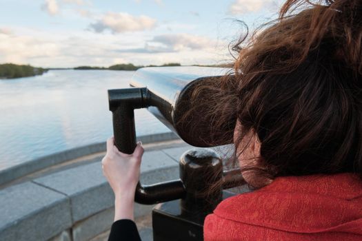 A young girl looks through a large city binoculars. City landmarks