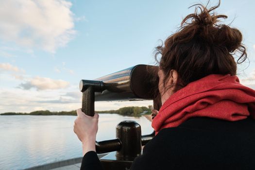 A young girl looks through a large city binoculars. City landmarks