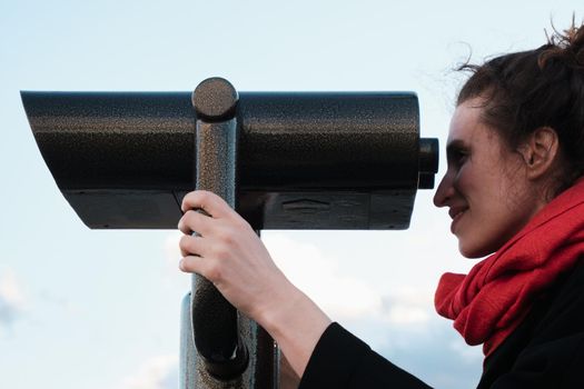 A young girl looks through a large city binoculars. City landmarks