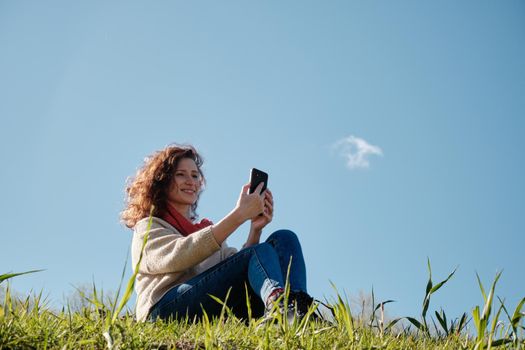 Young girl with a phone in her hands, green grass and blue sky