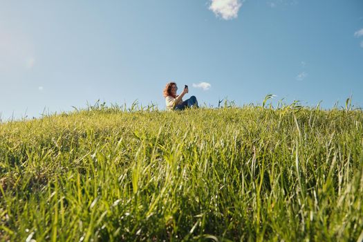 Young girl with a phone in her hands, green grass and blue sky