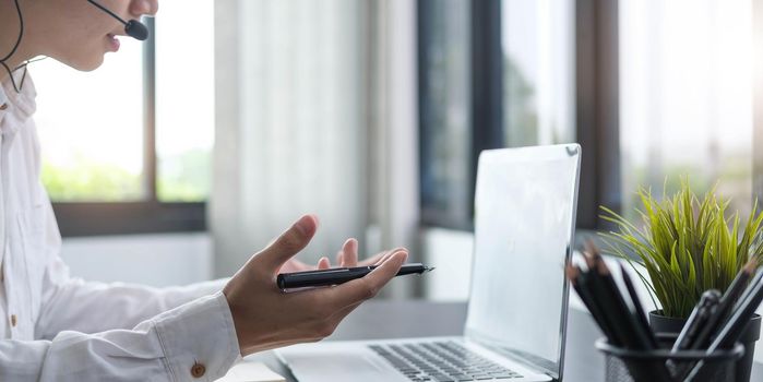 Focused young businessman manager wearing headset with microphone, involved in distant online meeting with colleagues or partners, discussing working issues using video call computer application..