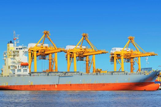 Container Cargo freight ship with working crane bridge in shipyard.
