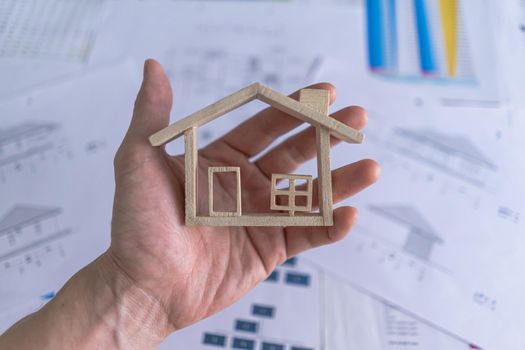 Top view. Hand holding miniature model house on background with the home design document, paperwork, contract agreement. The concept for sell, rent, loan home.