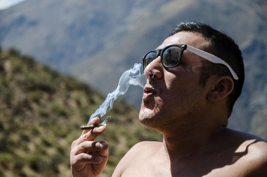 Young man smoking tobacco, man with sunglasses and mountains background