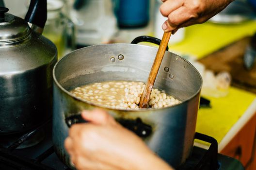 Beans cooking in a steel pot moving with a wooden spoon, home kitchen