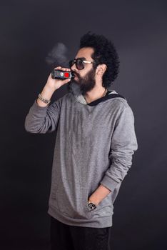 Vaping man holding a mod. A cloud of vapor. Black background. Vaping an electronic cigarette with a lot of smoke. Vape concept