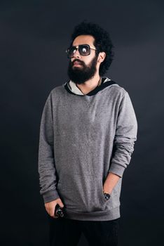 Thoughtful bearded young man with gray sweater and sunglasses. Man holding a mod. Black background.