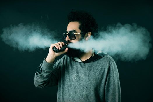 Vaping man holding a mod. A cloud of vapor. Black background. Vaping an electronic cigarette with a lot of smoke. Vape concept