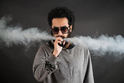 Vaping man holding a mod. A cloud of vapor. Black background. Vaping an electronic cigarette with a lot of smoke. Vape concept