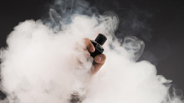 Hand of man soars on the smoke with mod in a black background. Vape concept