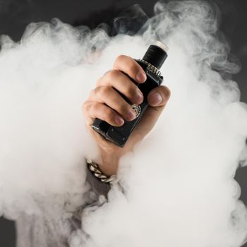 Hand of man soars on the smoke with mod in a black background. Vape concept