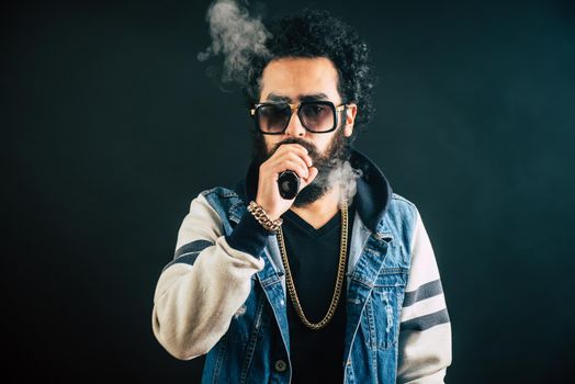 Young man with beard and sunglasses vaping an electronic cigarette. Vaper hipster smoke vaporizer