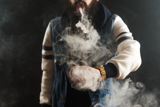 Young man with beard throwing a cloud of steam. Black background. Vaping an electronic cigarette with a lot of smoke