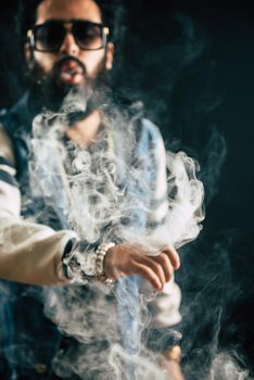 Young man with beard throwing a cloud of steam. Black background. Vaping an electronic cigarette with a lot of smoke