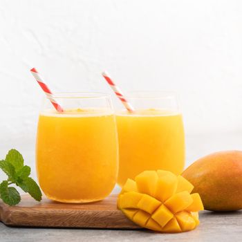 Fresh beautiful delicious mango juice. Close up design concept of smoothie cold drink in a glass cup with paper straw on gray table background.