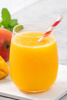 Fresh beautiful delicious mango juice. Close up design concept of smoothie cold drink in a glass cup with paper straw on gray table background.