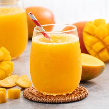 Fresh beautiful delicious mango juice. Close up design concept of smoothie cold drink in a glass cup with paper straw on gray table background.